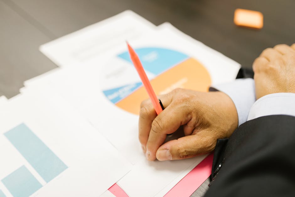 A businessman writing on financial documents with charts in an office setting.